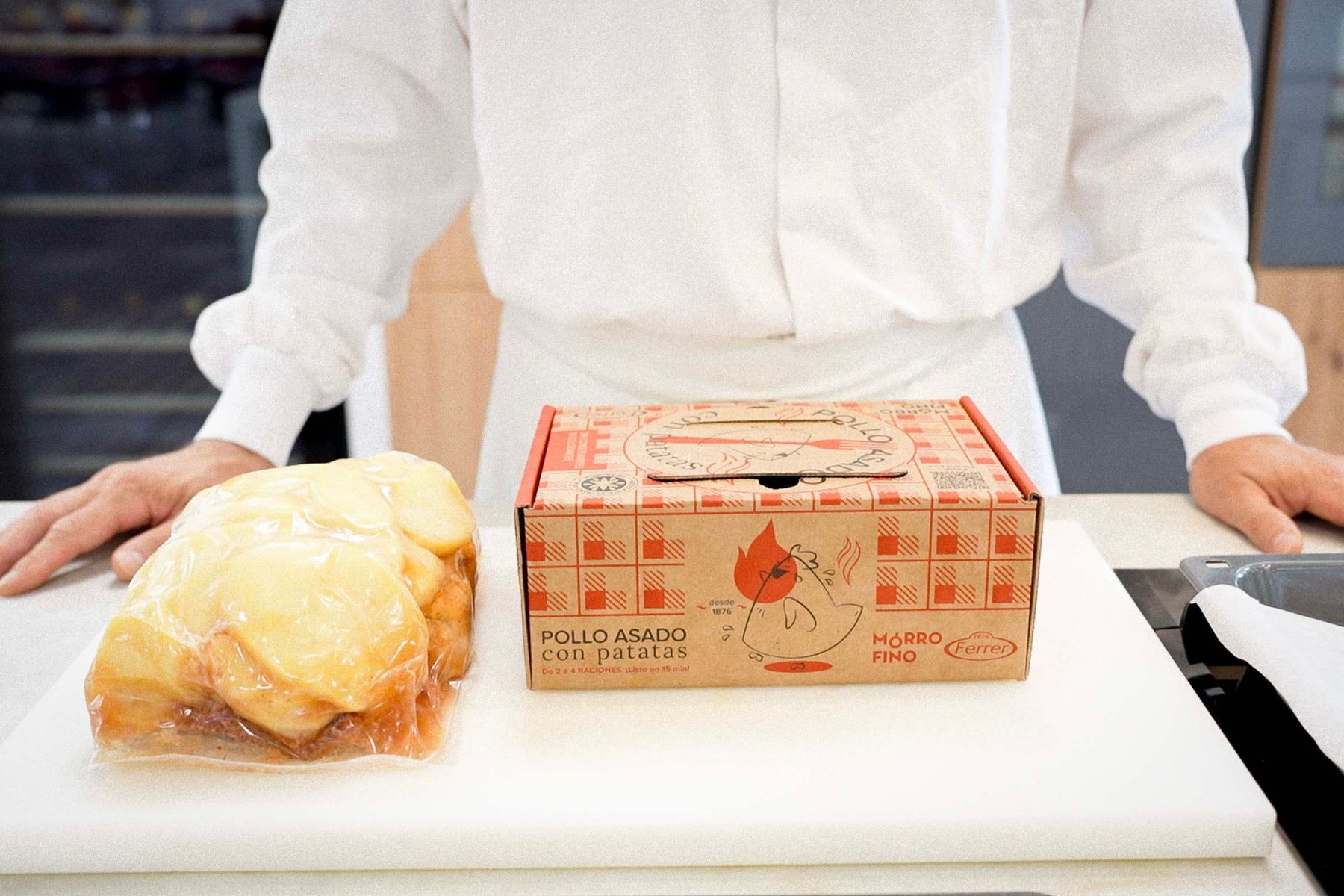 Caja del pollo asado Mórrofino con Antoñito junto al pollo envasado, en la cocina